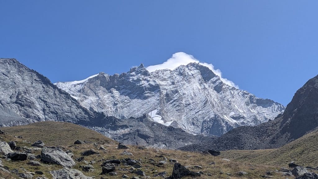 Montagne enneigée sous ciel bleu, premiers plans rocheux et herbeux.