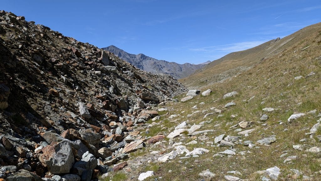 Vallée alpine ensoleillée, flanc rocheux et herbeux sous ciel bleu.