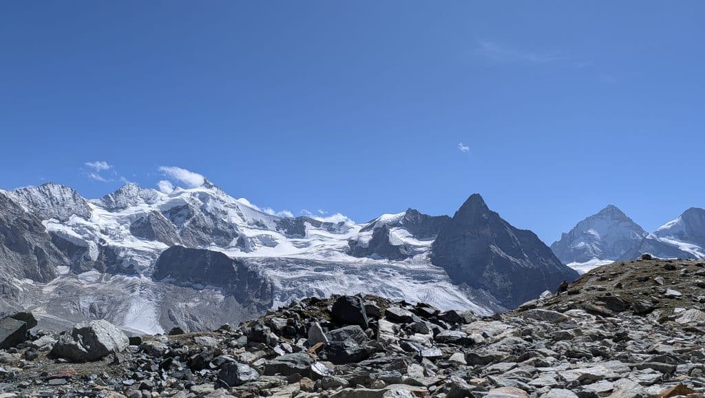 Montagnes enneigées, glaciers et terrain rocheux sous ciel bleu.