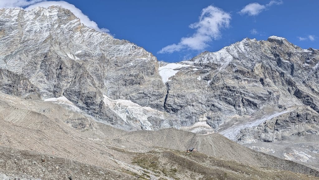 Refuge de montagne isolé devant d'imposants sommets enneigés et glaciers.