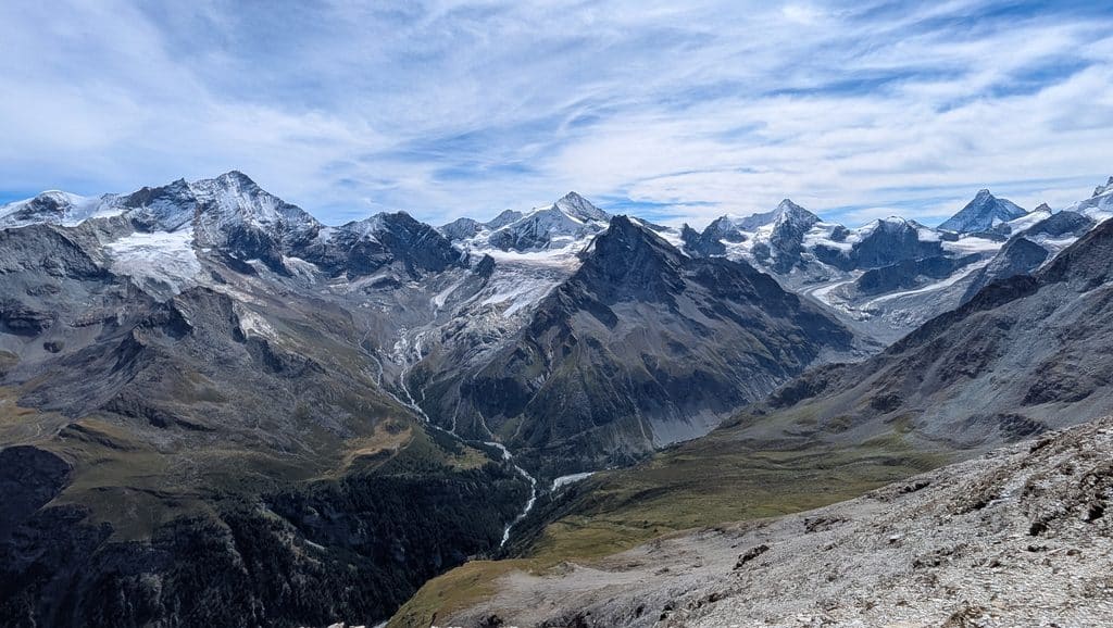 Chaîne de montagnes enneigées, glacier, vallée fluviale et ciel nuageux.