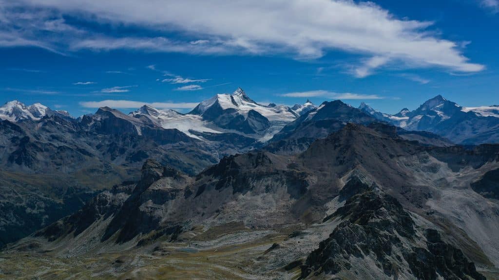 Vaste chaîne de montagnes, sommets enneigés et glaciers sous ciel bleu.