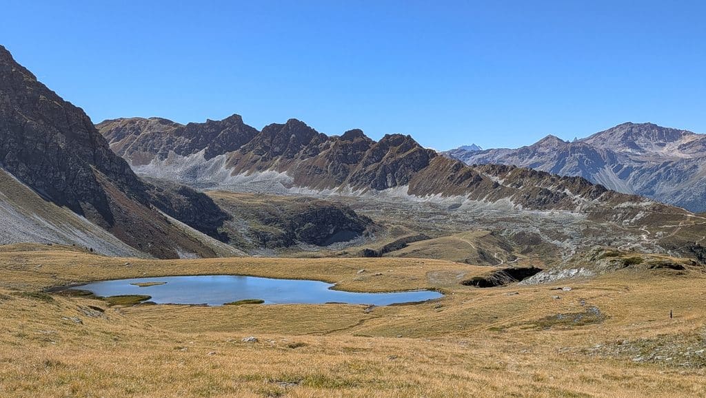 Lac alpin entouré de montagnes et herbe sèche sous ciel bleu.