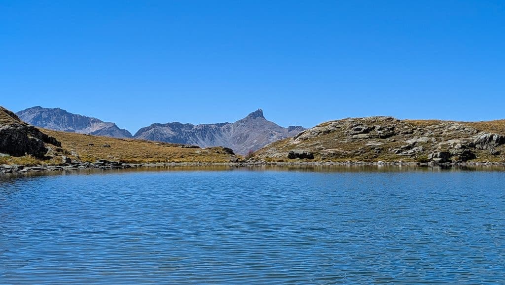 Lac de montagne, ciel bleu, sommets rocheux, paysage alpin.
