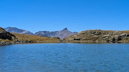 Lac de montagne, ciel bleu, sommets rocheux, paysage alpin.