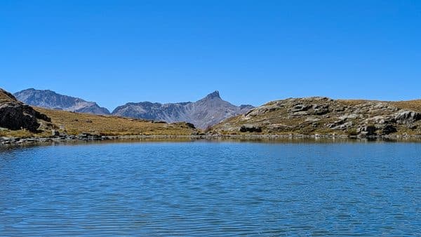 Lac de montagne, ciel bleu, sommets rocheux, paysage alpin.