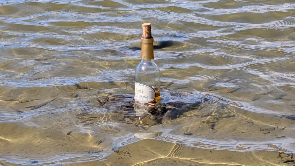 Bouteille en verre bouchée flottant dans l'eau claire peu profonde.