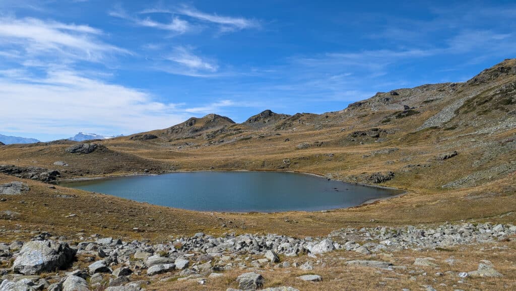 Lac alpin serein entouré de montagnes rocailleuses sous ciel bleu.
