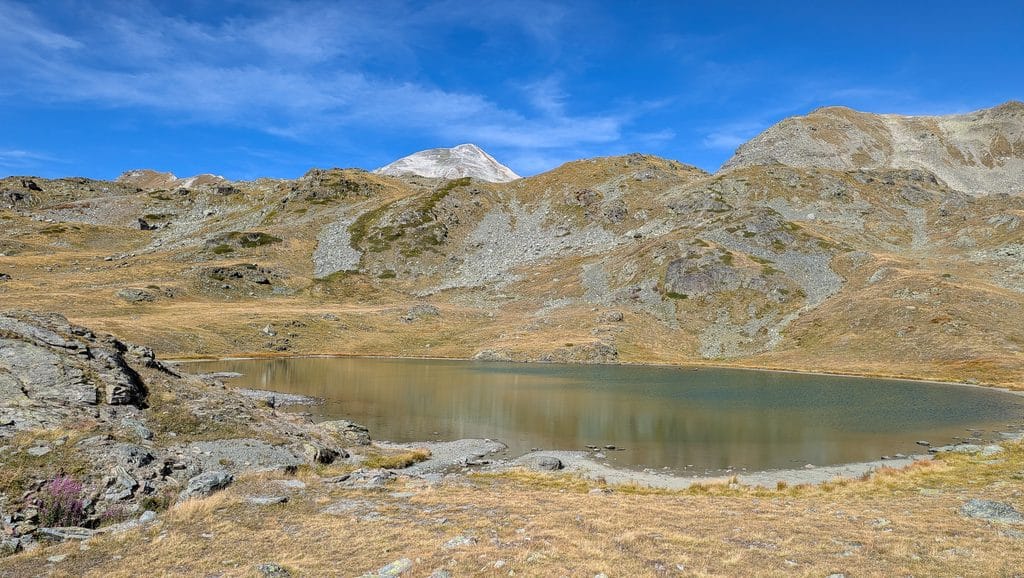 Lac de montagne, herbe sèche, ciel bleu, sommets rocheux.