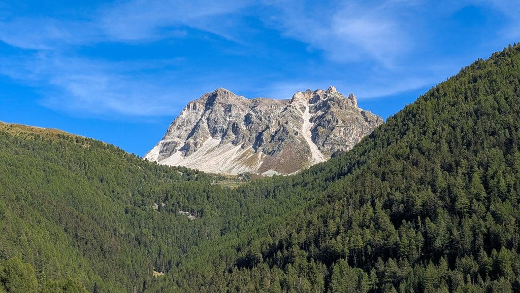 Montagne rocheuse majestueuse, forêts de pins sous ciel bleu alpin.